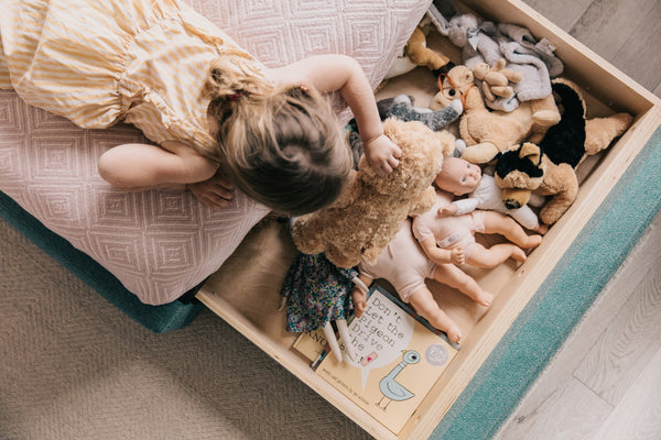 a twin bed with a pull out drawer at the foot of the bed for storage. Drawer is photographed open with books and dolls and a 5 year old girl looking into the drawer