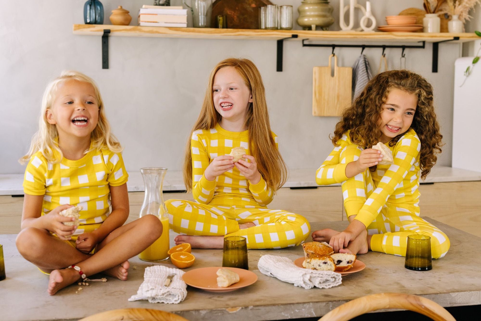 three girls wearing comfortable pajama sets in yellow gingham by la paloma eating breakfast in the morning