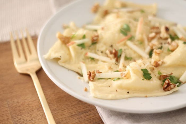 apple and walnut ravioli on a white plate with a gold fork