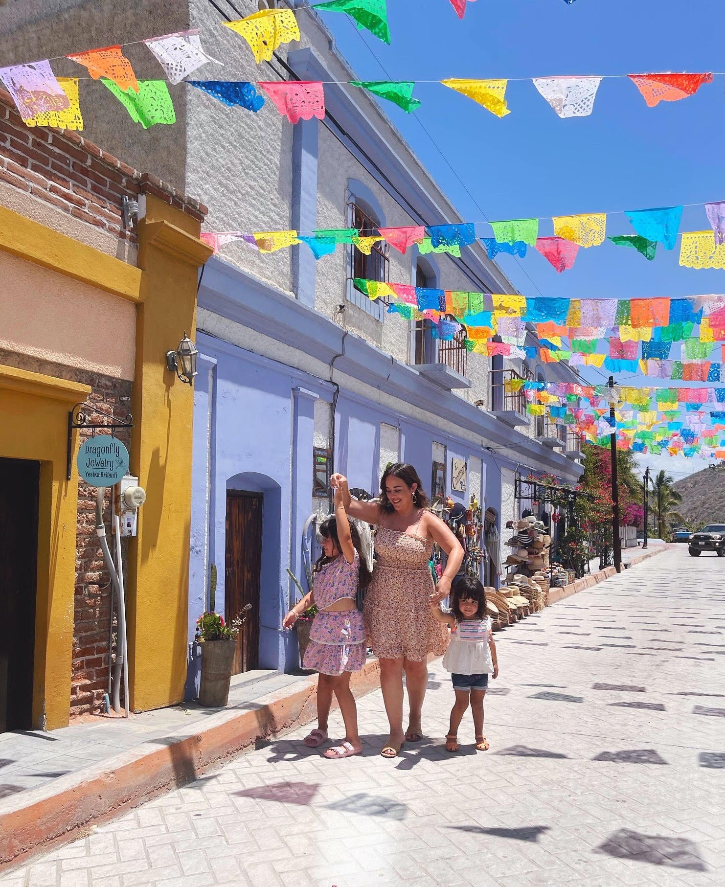 mom and two daughters in mexico in the summer with papel picado banners across the cobblestone streets