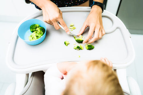 Mom crushing broccoli on baby's high chair table to practice EMR.