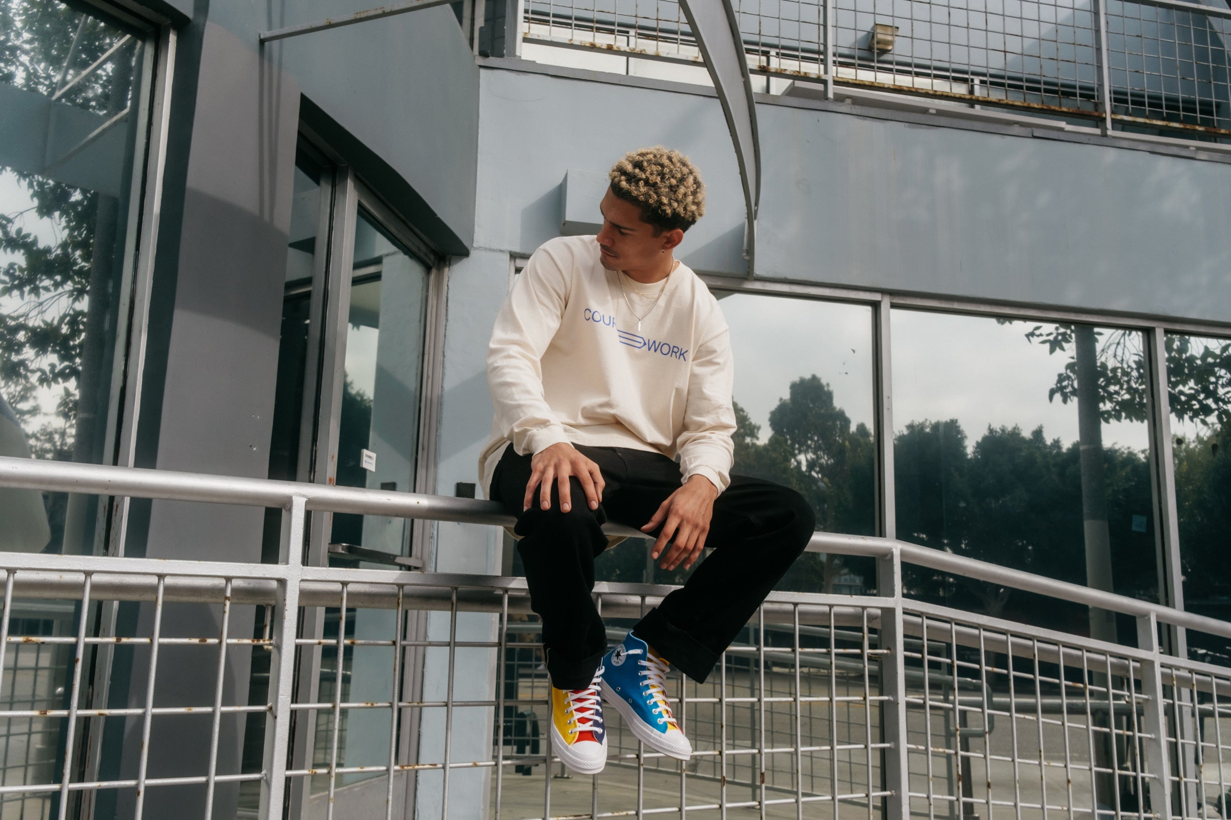 Model wearing the Full Width Text Long Sleeve Tee and sitting on a handrail.