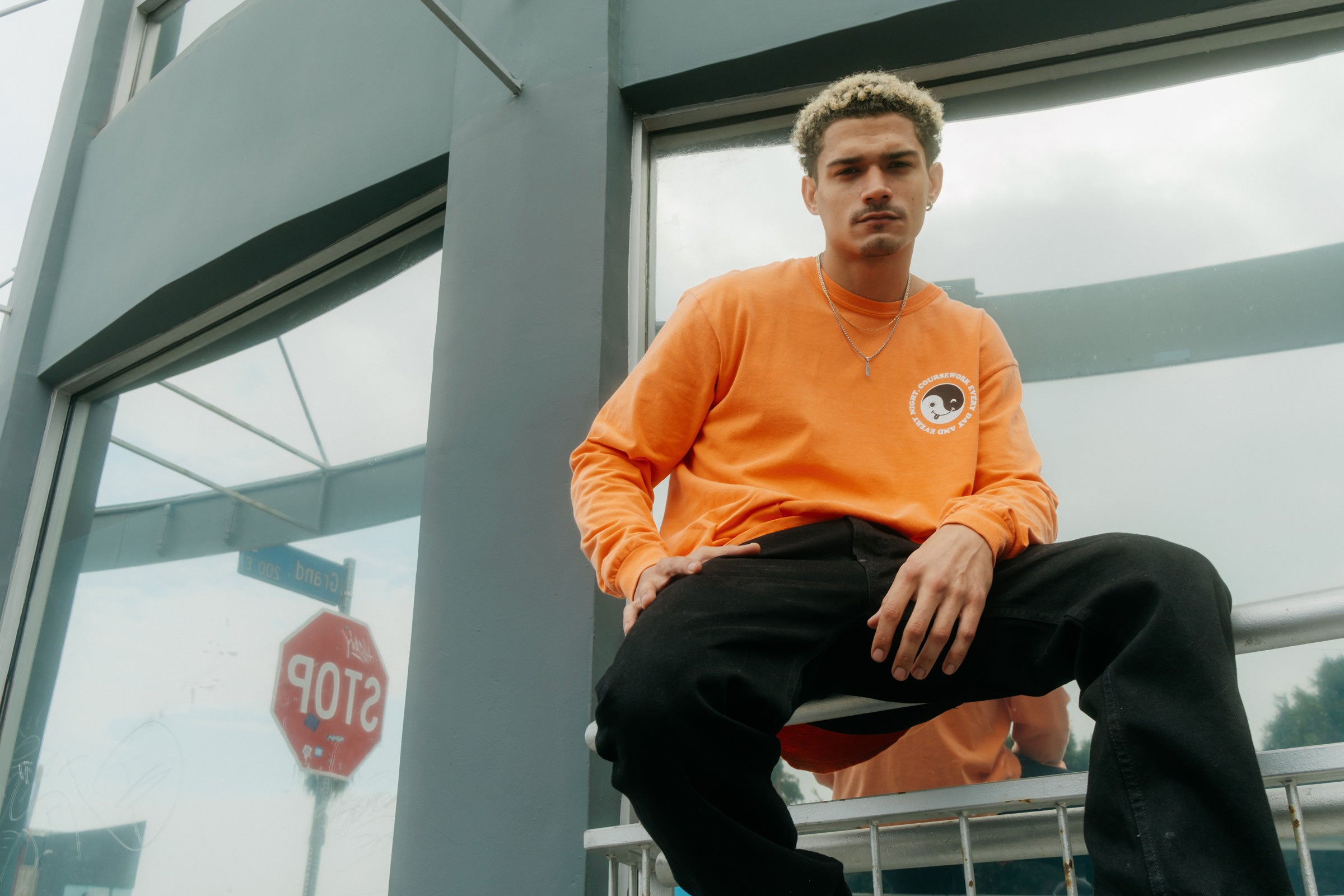 Model wearing the Day and Night Long Sleeve Tee in orange and sitting on a handrail.