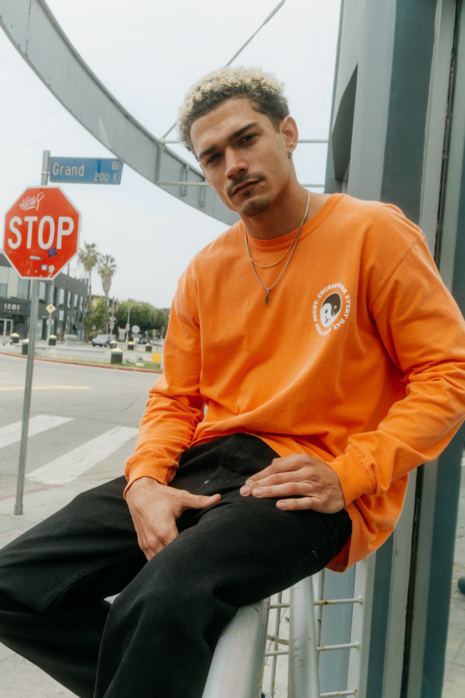 Model wearing the Day and Night Long Sleeve Tee in orange and sitting on a handrail.