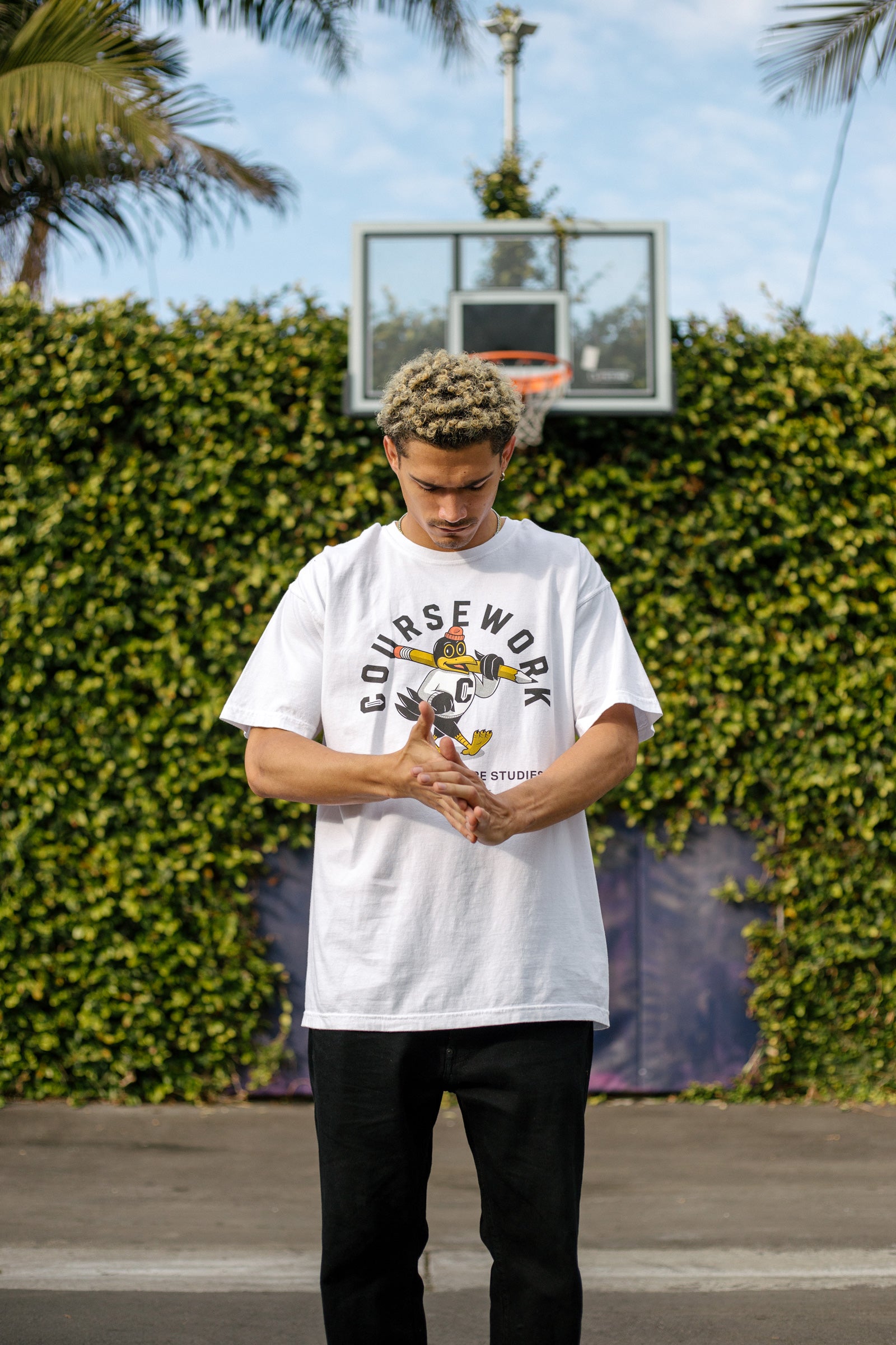 Model wearing the Early Birds tee with a basketball hoop and green foliage behind him.