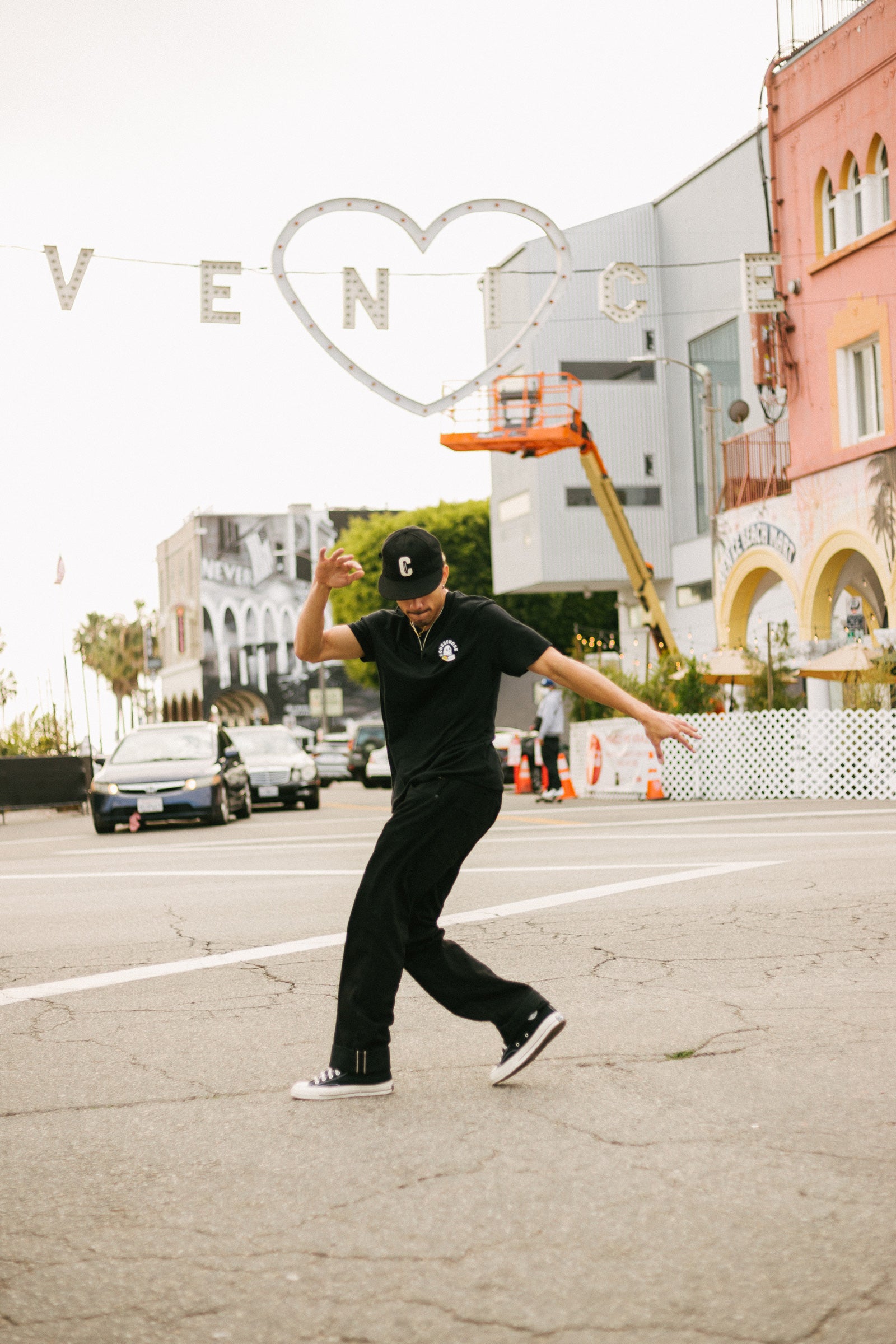 Model wearing the Ebbets Wool C Cap in black and the Required Reading Tee in black while breakdancing in the street.