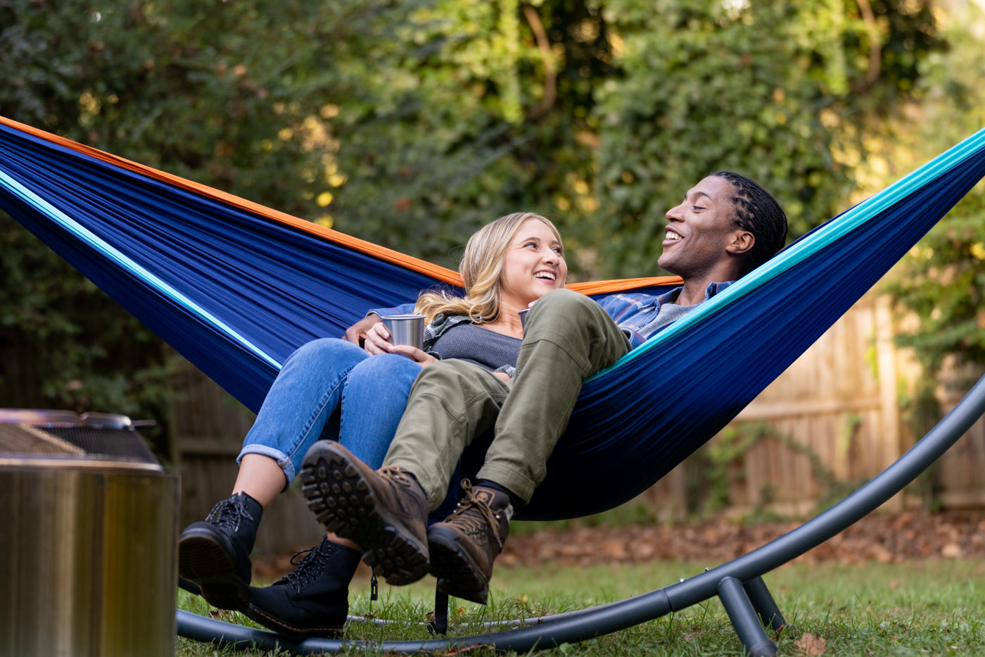 Two people share an ENO DoubleNest Hammock in a backyard.