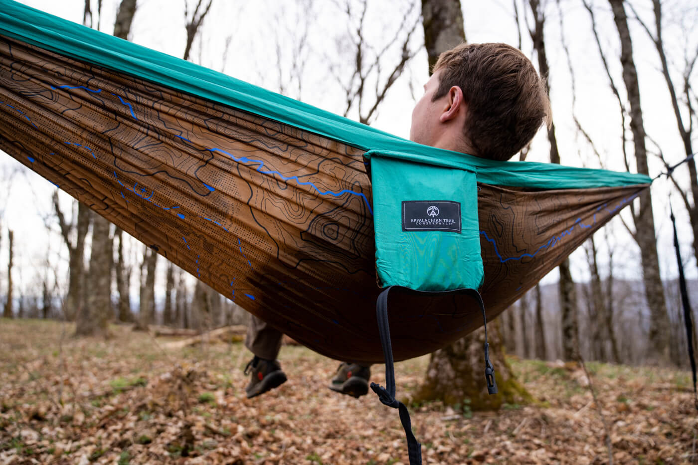 A man sits in an ATC Giving Back Hammock Print while in the woods.