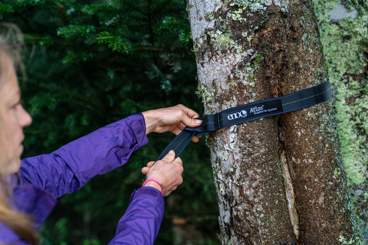 A woman sets up her Atlas Hammock Straps around a tree. 