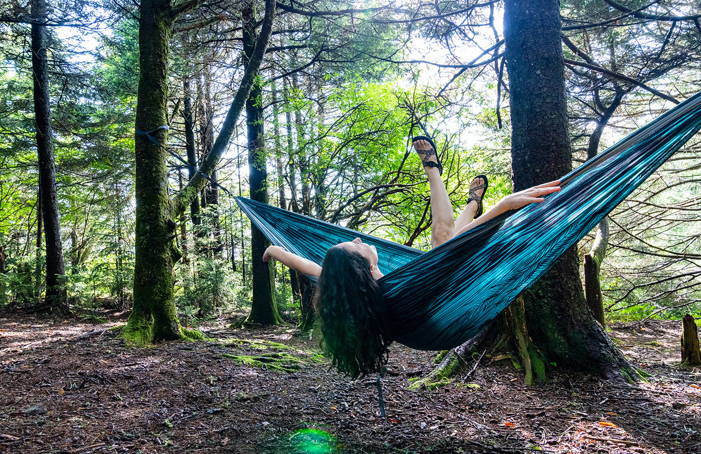 A woman leans back while sitting in a Mountains to Sea DoubleNest Print Hammock from ENO. 
