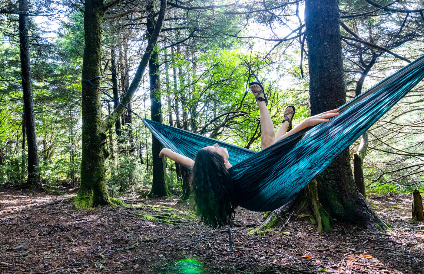 A woman tilts back in her ENO print hammock in the woods, surrounded with joy