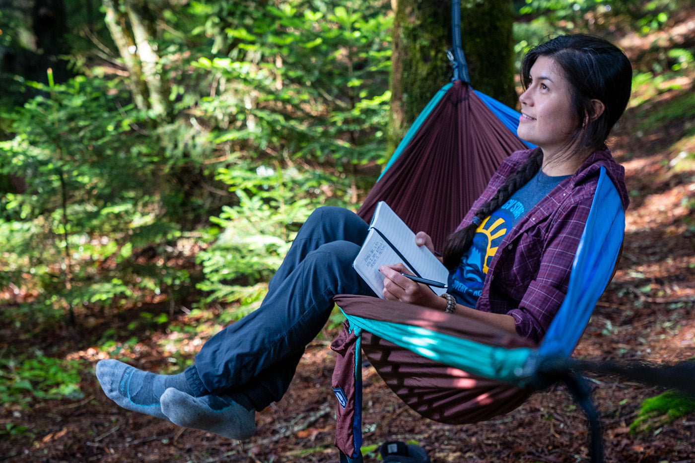 A woman sits in a tri-color ENO hammock with a journal. 