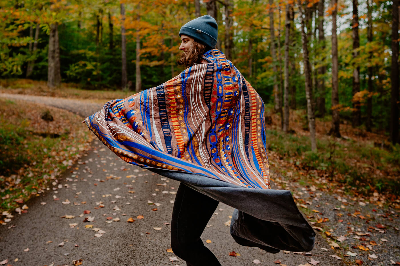 A woman twirls in the road, surrounded by fall foliage while wearing her ENO FieldDay Blanket