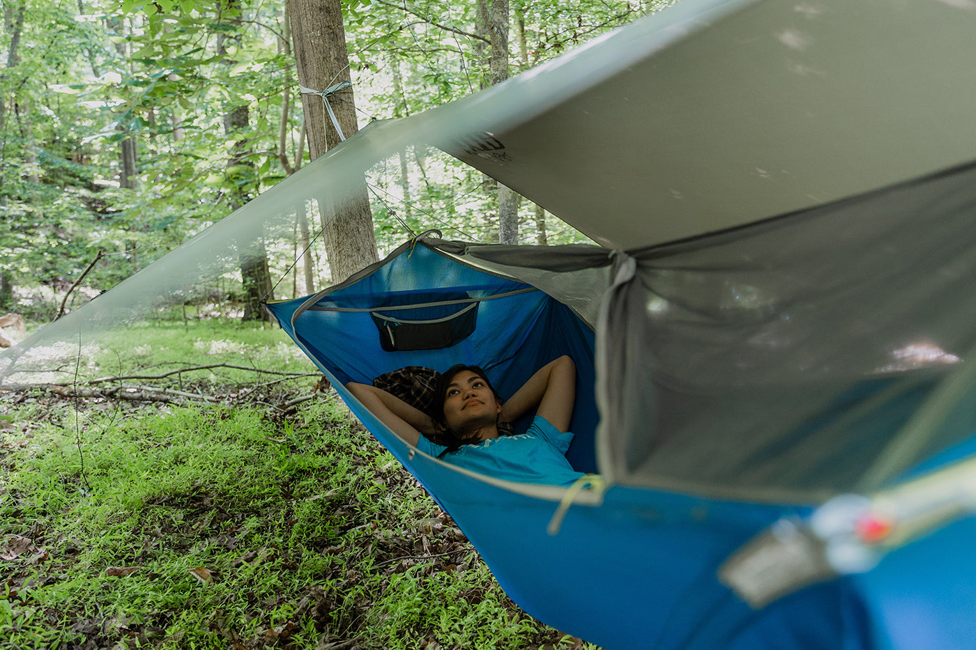A woman lays in her SkyLite hammock protcted by a rain tarp while hammock camping