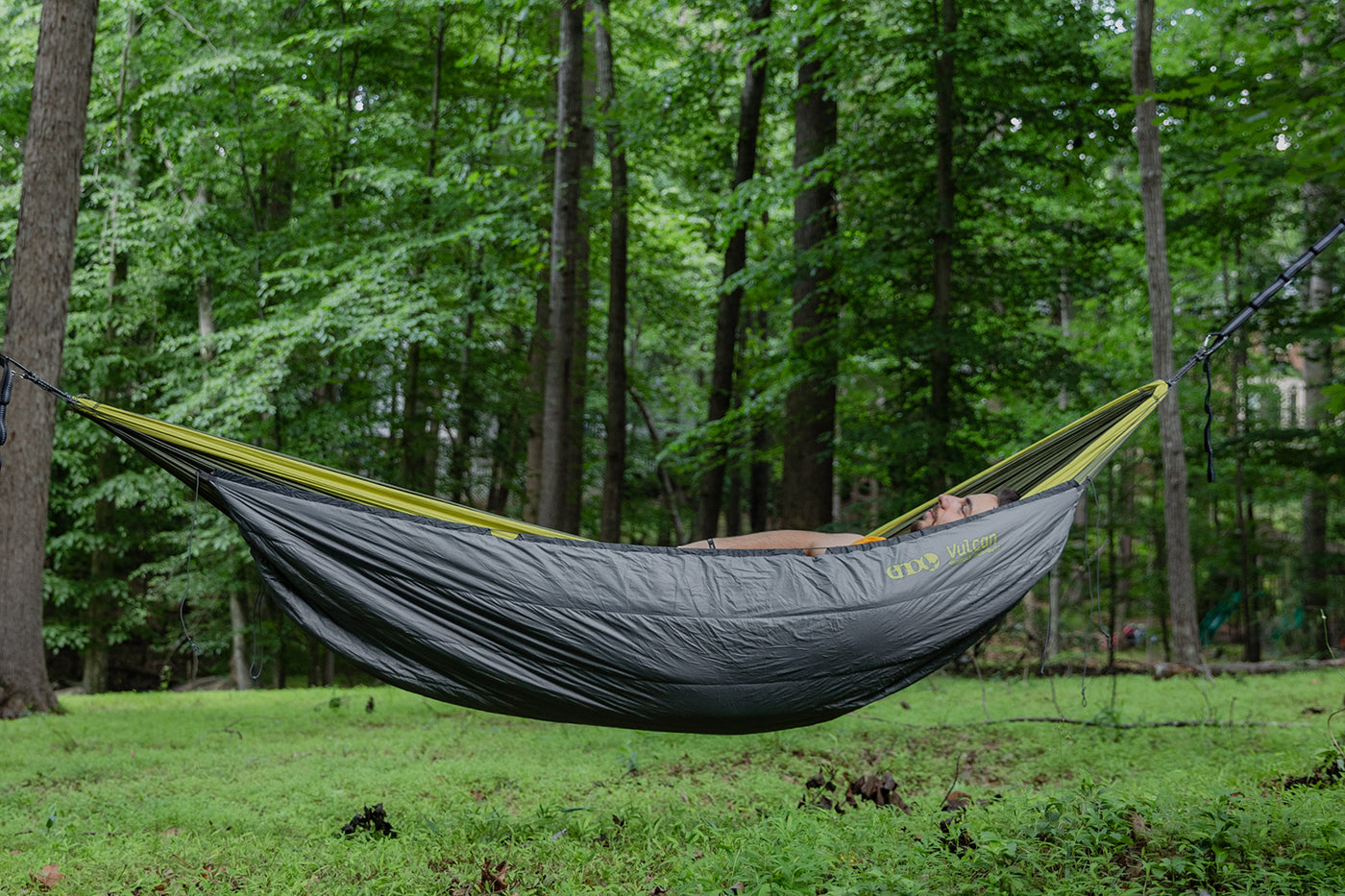 A man lays in a DoubleNest Hammock using a Vulcan UnderQuilt to keep warm.