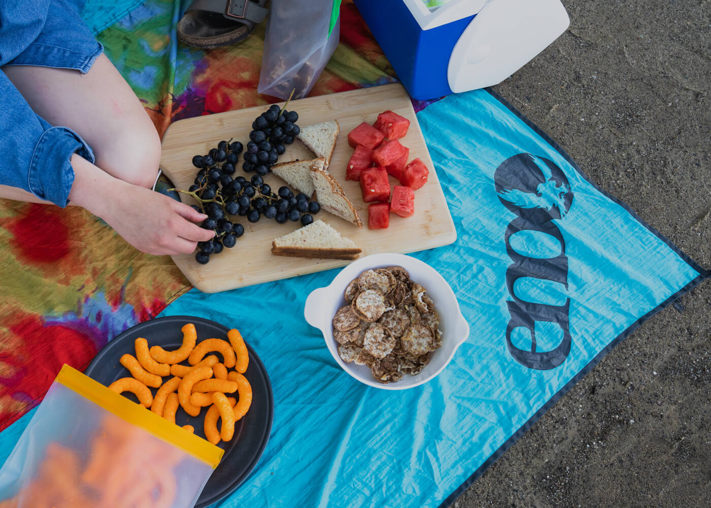 Two people share a picnic using an ENO Islander Blanket Print covered in snacks. 