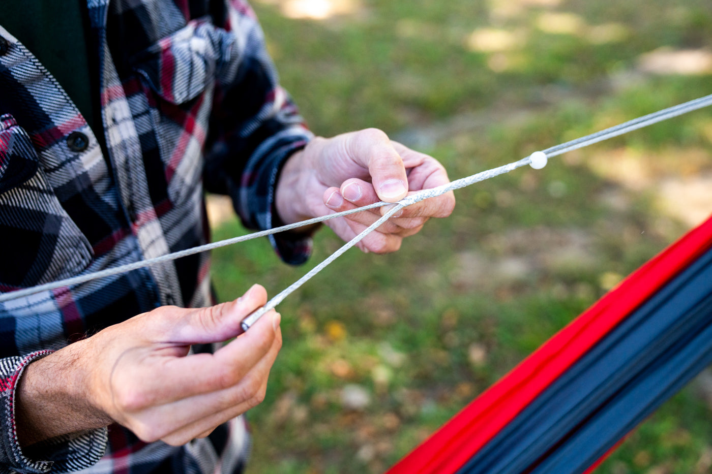 A man adjusts the length of the Microtune Structural Ridgeline on a hammock to get the ideal hang. 