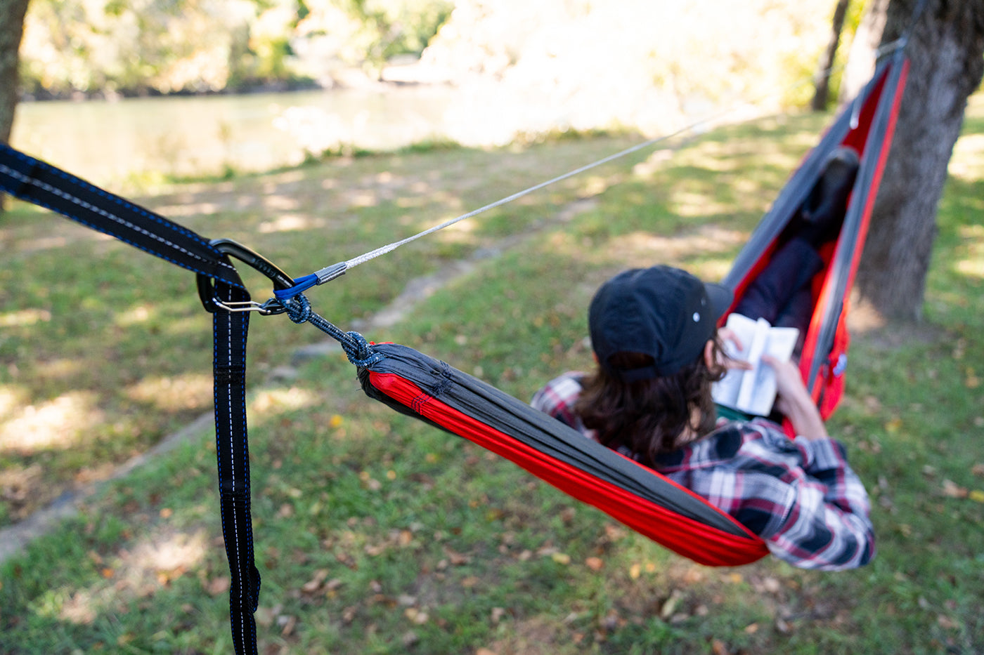 A man lays in a red and charcoal ENO hammock while using the Microtune Structural Ridgeline. 