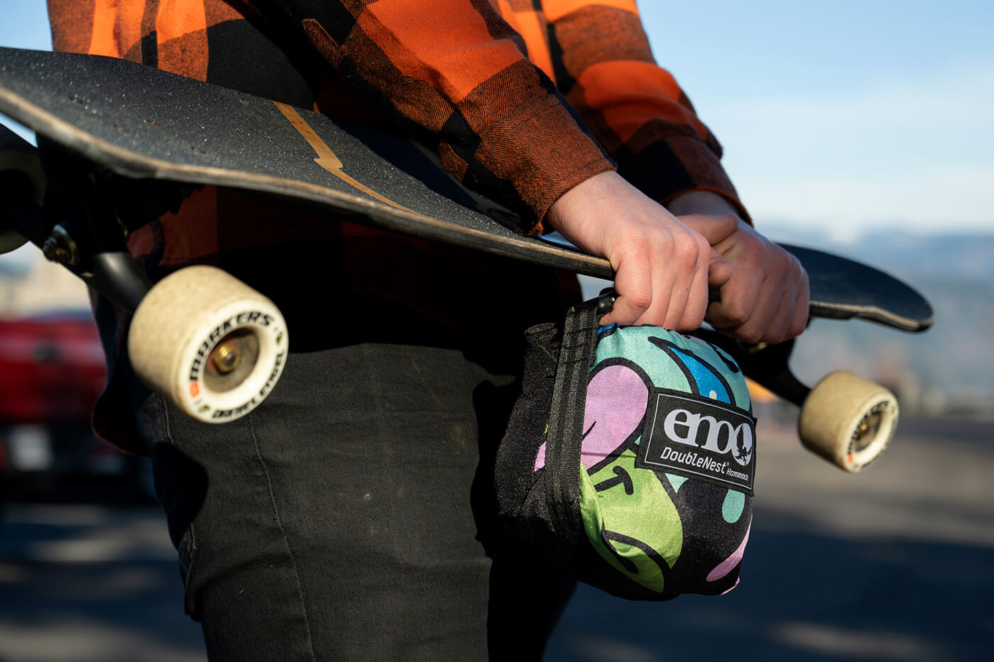 A person holds the Nature Talk Hammock stuff sack while also holding their skateboard. 