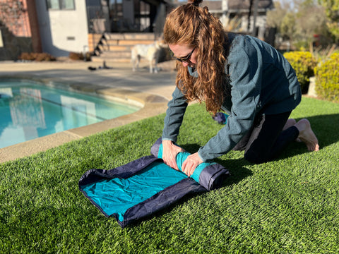 A woman packs up the Lounger GL by rolling the fabric on the grass. 