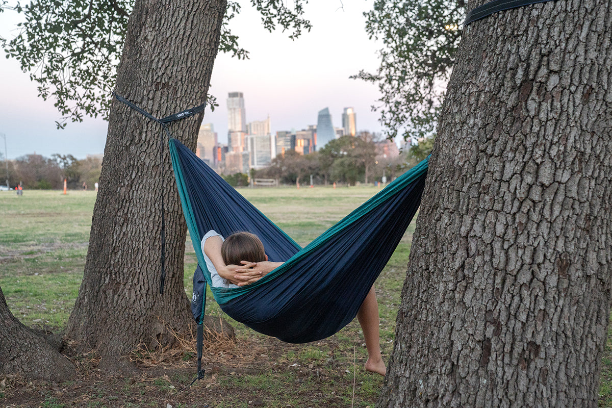 Paige Pierce relaxes in a hammock while at a park, looking at a city skyline.