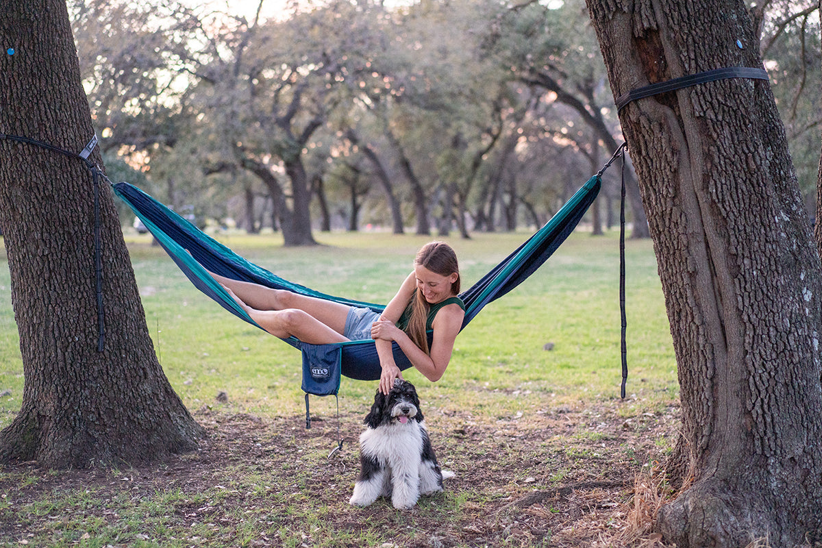 Paige Pierce lays in an ENO DoubleNest hammock while petting her dog sitting beside her.