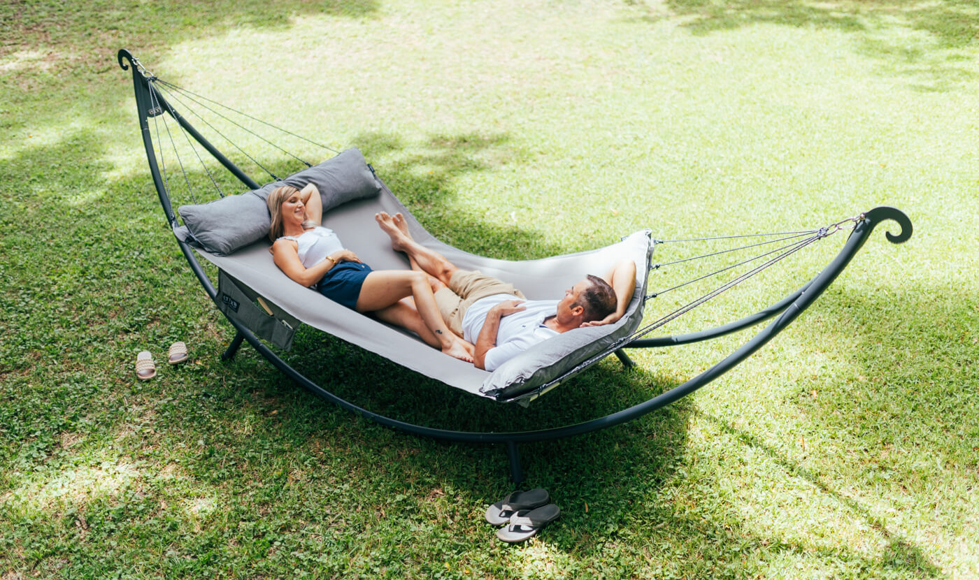 A woman and man share a SuperNest SL Hammock in their backyard