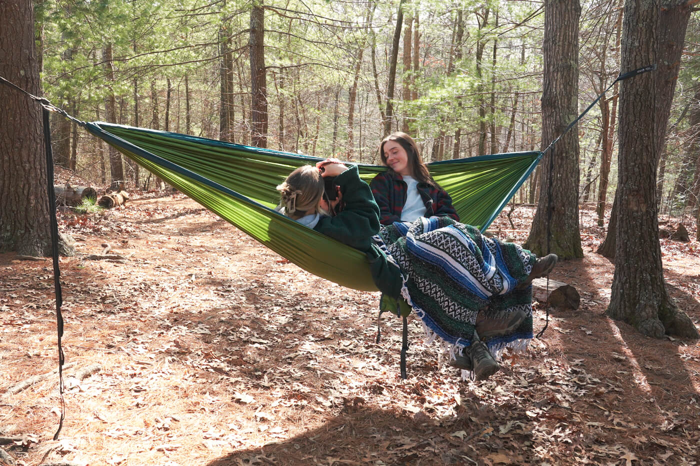 Two women share an ENO DoubleNest hammock as one takes a photo of the other. 