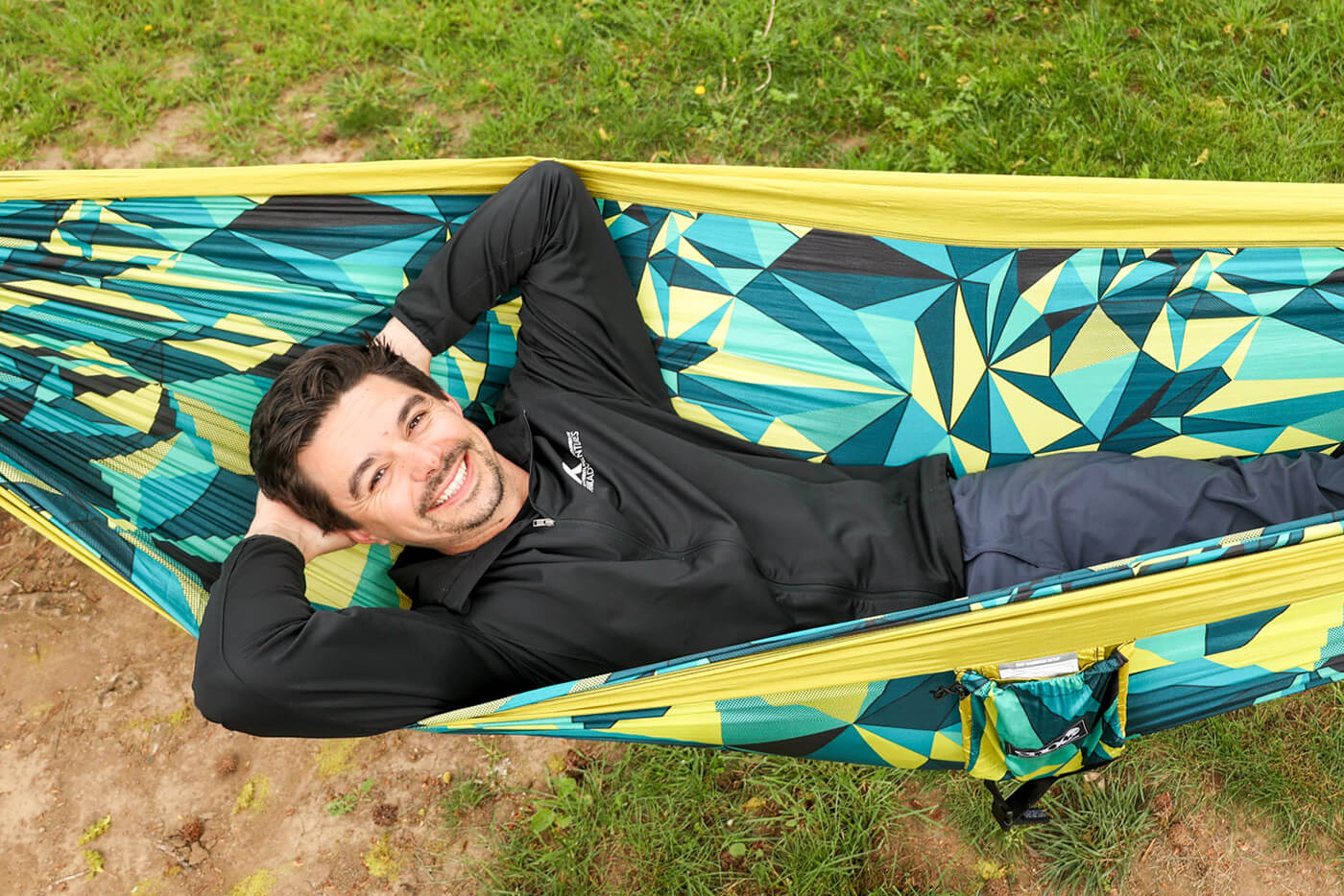 A man lays in an ENO DoubleNest Hammock Print in Boulder as he smiles for his picture. 