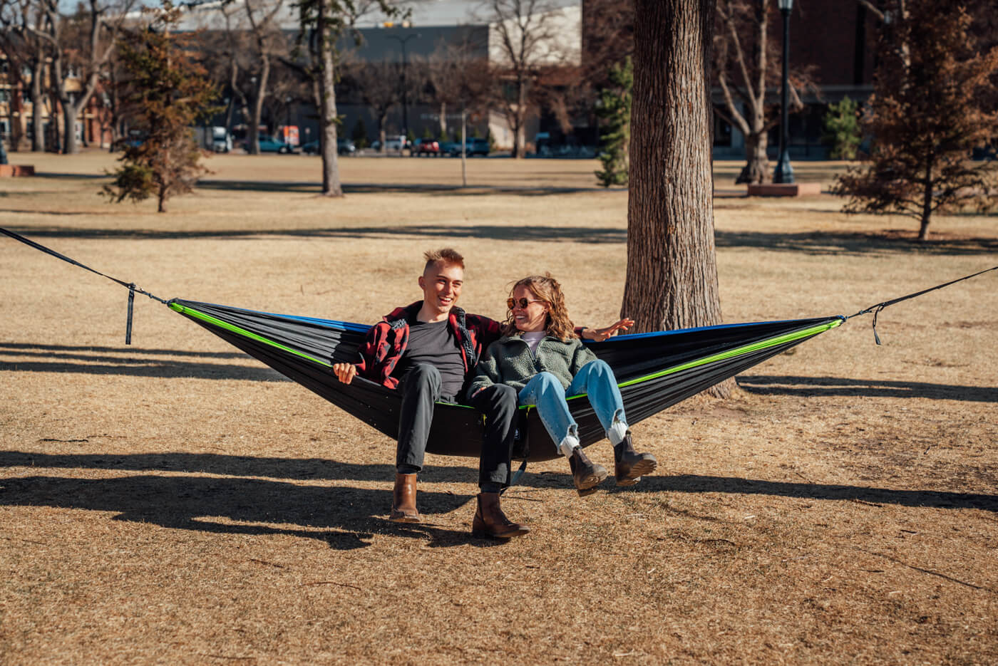 A man and woman share a DoubleNest hammock on a college green.