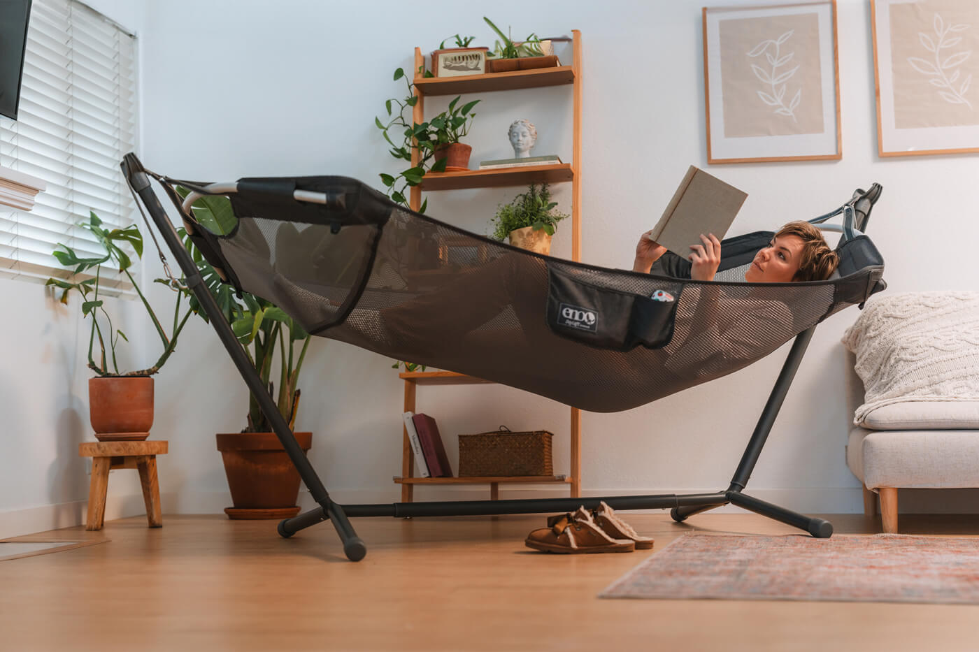 A woman uses her DayLoft Hammock indoors paired with her Parkway Adjustable Hammock Stand. She reads a book.