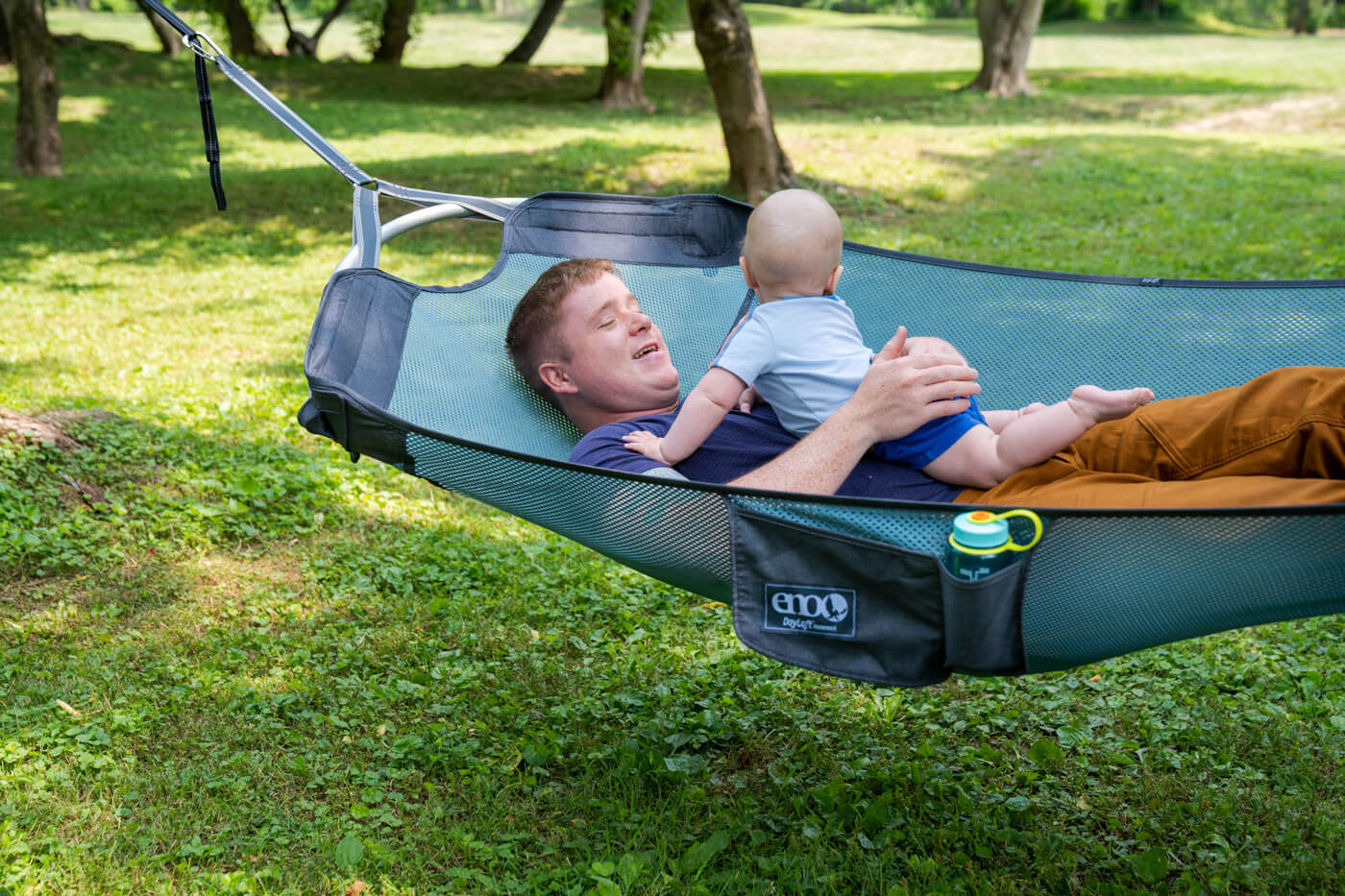 A dad holds his baby while laying in the DayLoft Hammock.