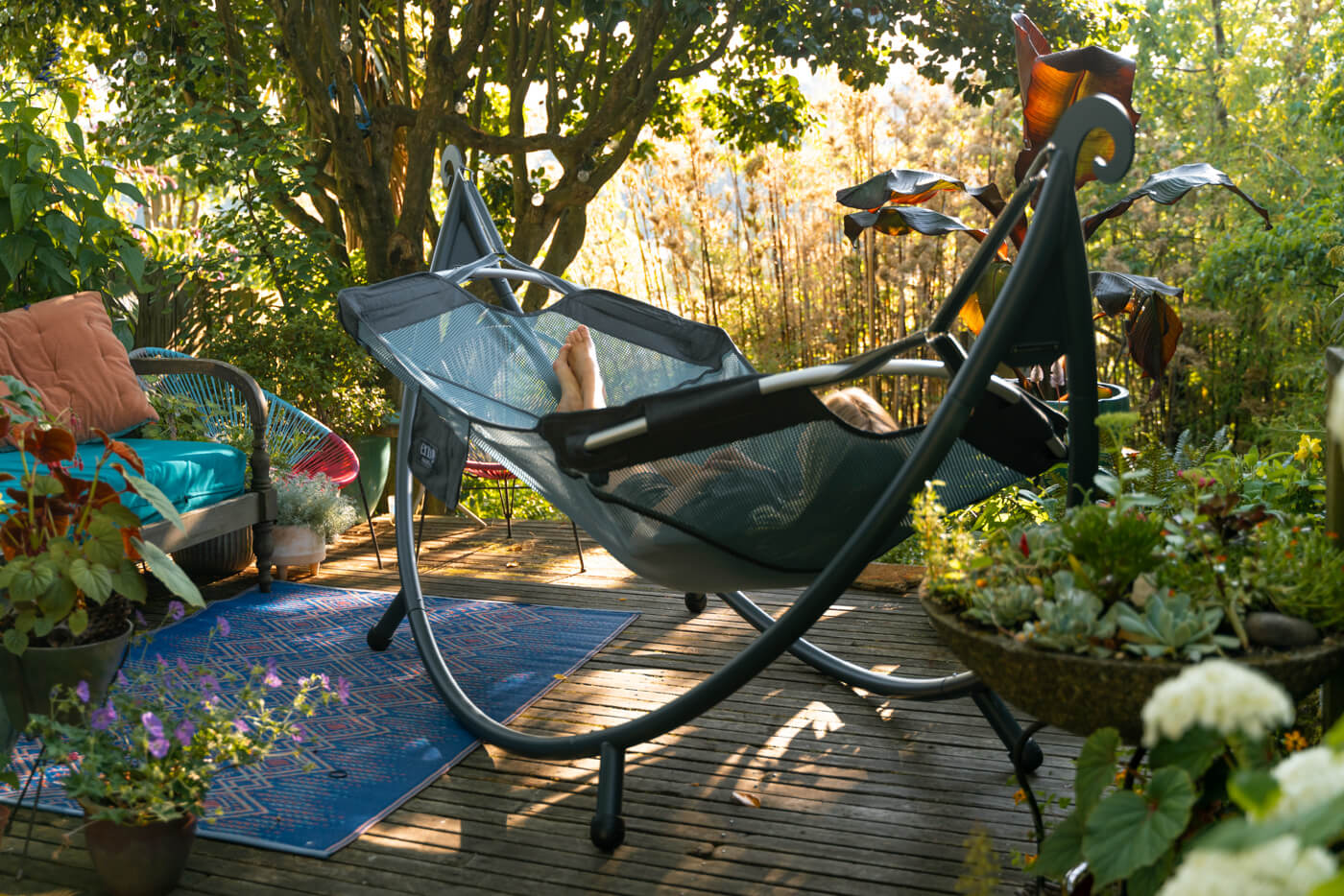 A person lays in the DayLoft Hammock while on their back porch surrounded by plants.