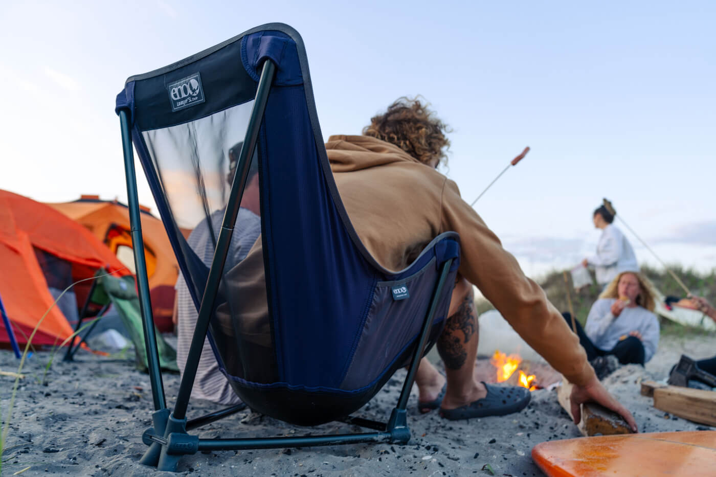 A man sits in an ENO Lounger SL Chair while cooking on the beach.