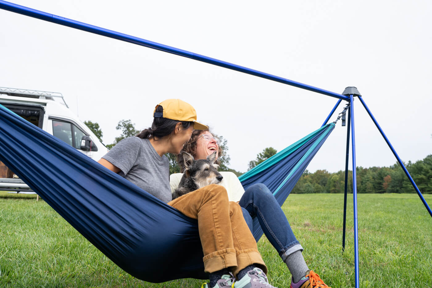 Two people share a hammock while relaxing in a Nomad Hammock Stand while traveling in their van.
