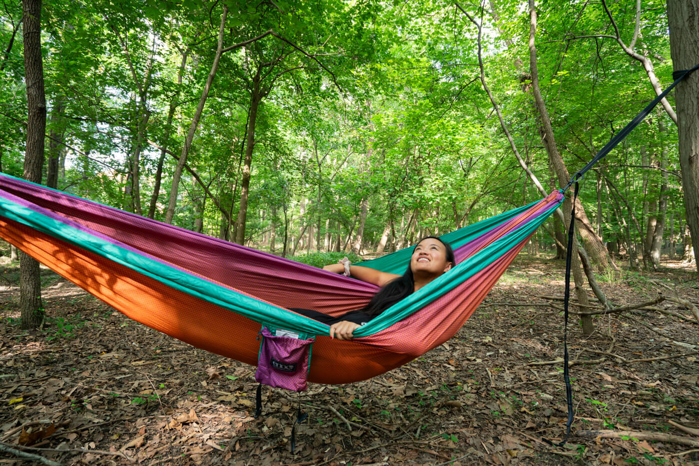 A woman lays in an ENO DoubleNest Print Hammock in Fade while surrounded by lush green forest.