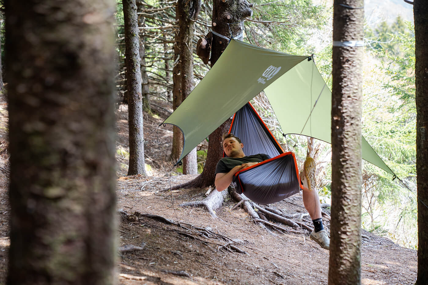 A man lays in his hammock camping setup near the base of Black Balsam Knob near the Blue Ridge Parkway while in a dense forest of pine trees