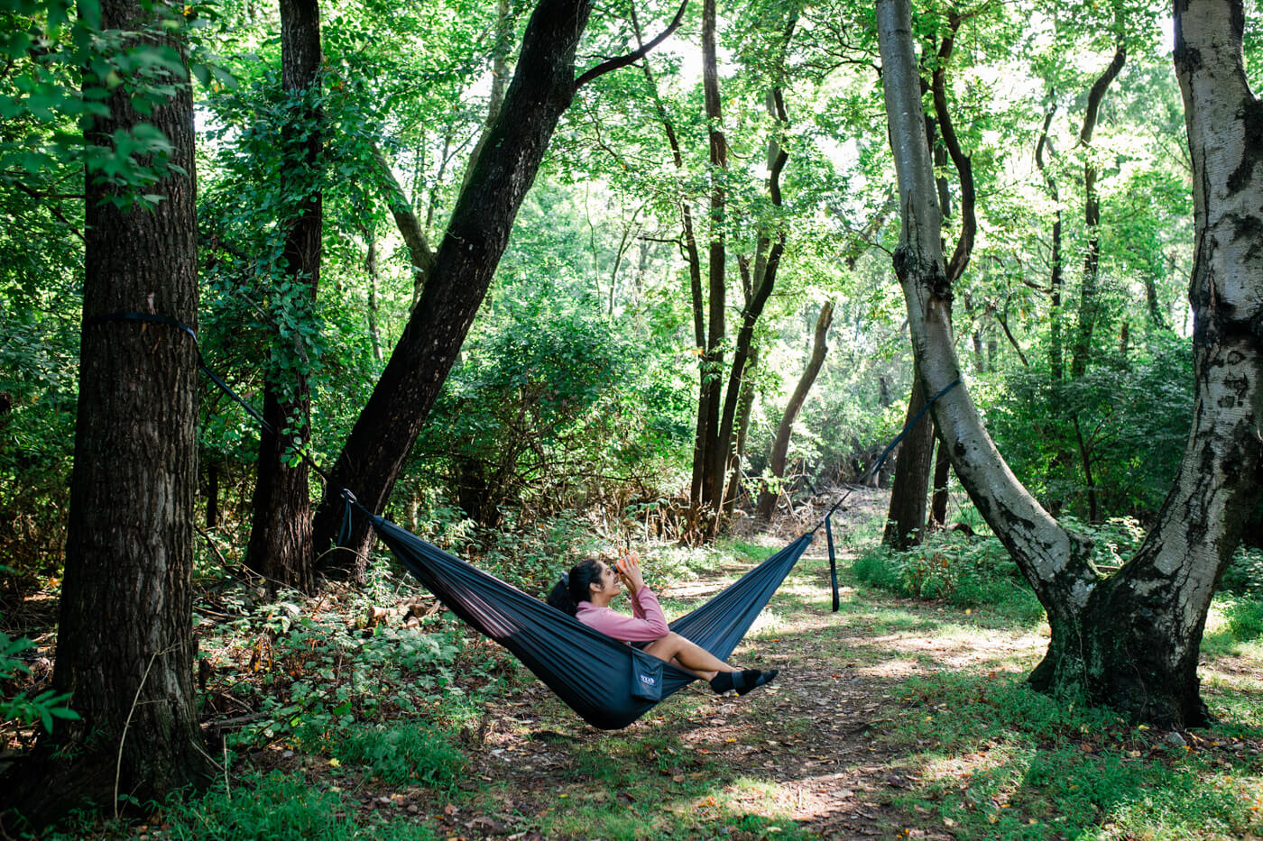 A woman uses binoculars while sitting in her ENO TravelNest Hammock and Straps Combo