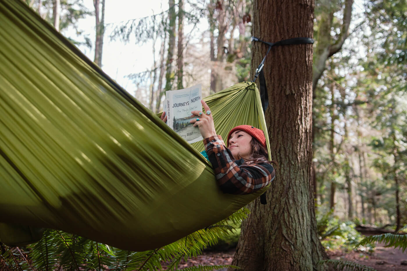 A woman reads a book while relaxing in her TravelNest Hammock + Straps Combo