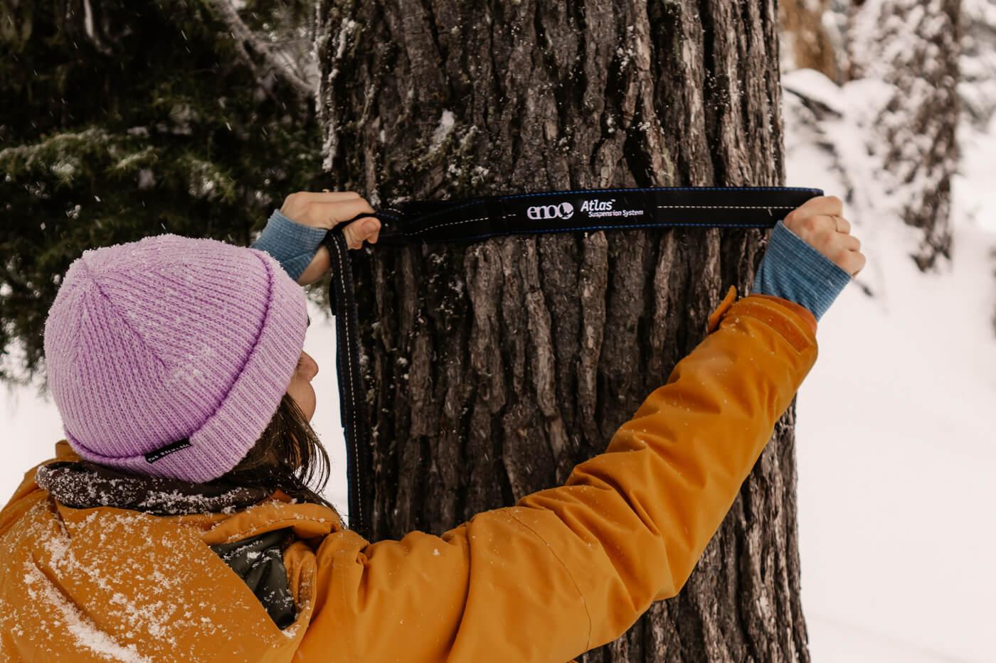 A woman sets up her ENO Atlas Hammock Strap while surrounded by a snowy wonderland.