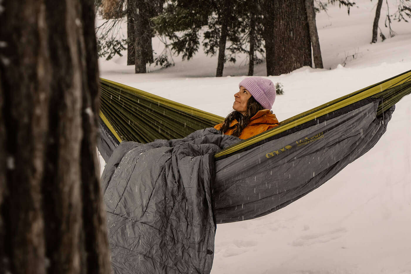 A woman sits in her hammock with insulation while surrounded by a winter wonderland. 