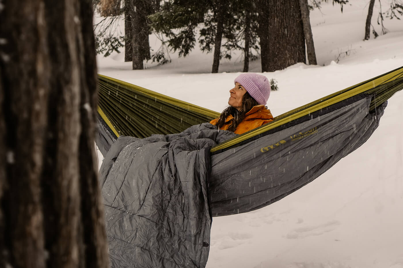 A woman sits in her ENO Hammock with the Vulcan and Vesta insulation keeping her warm on a snowy day