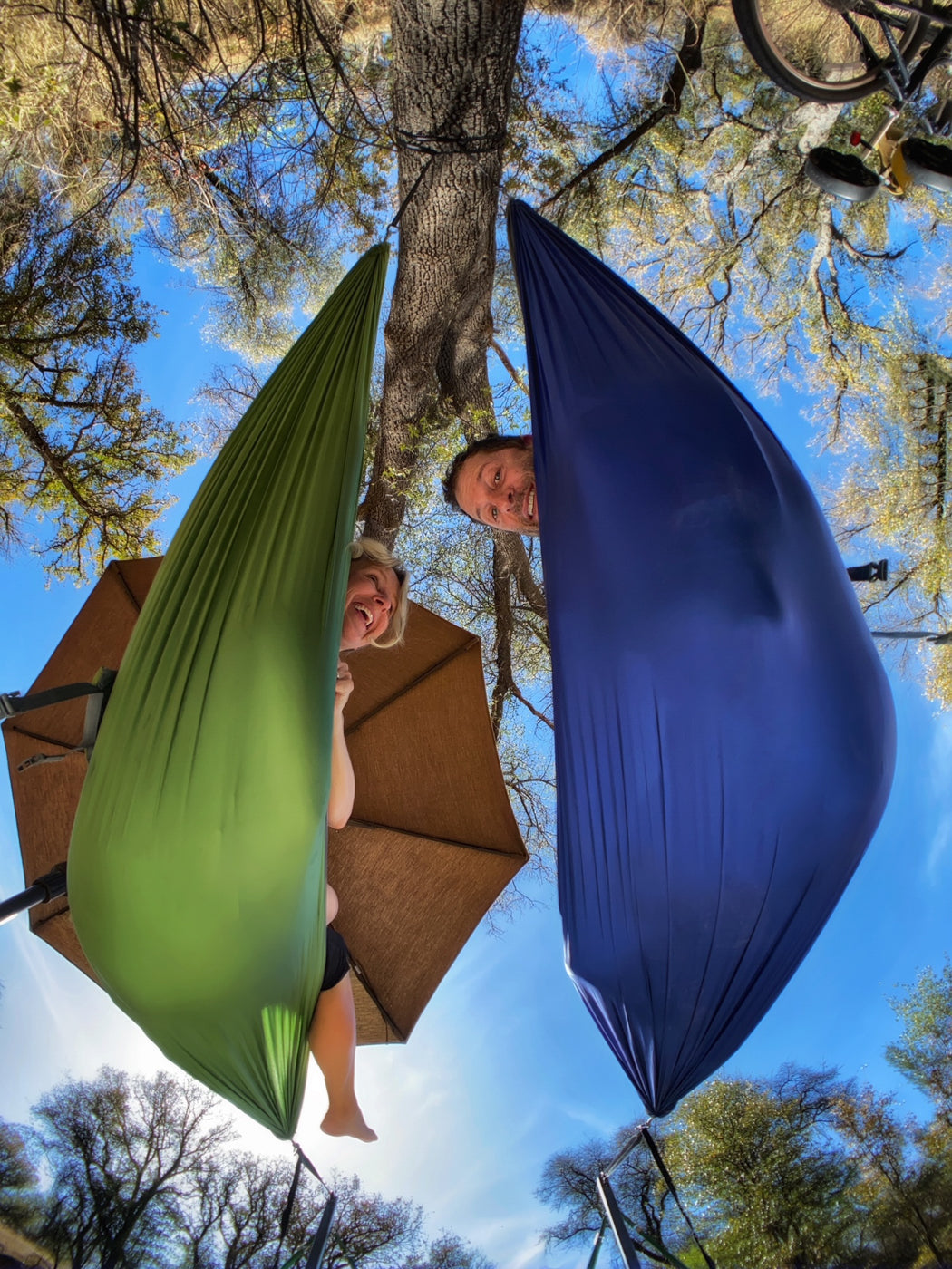 A view from below of two people hammocking together in their backyard. 