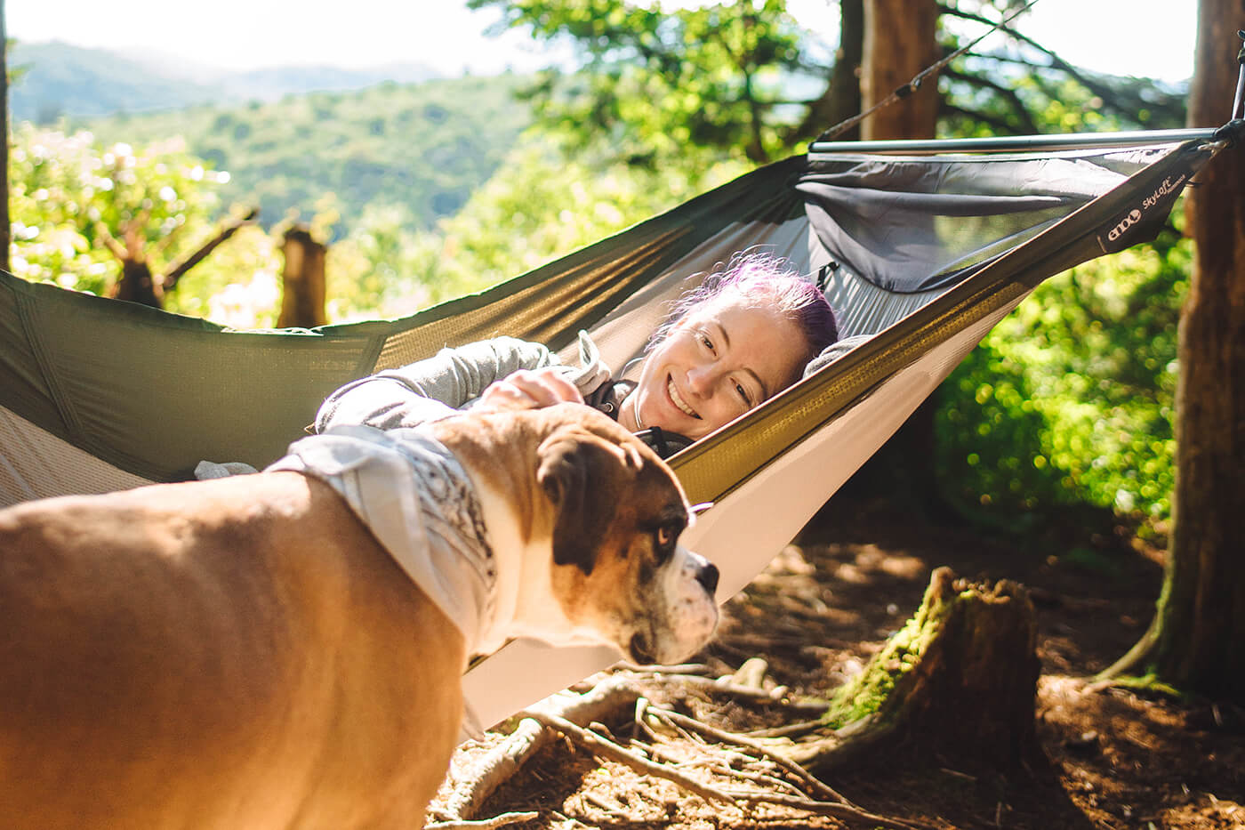 A woman pets a dog while in a SkyLoft hammock