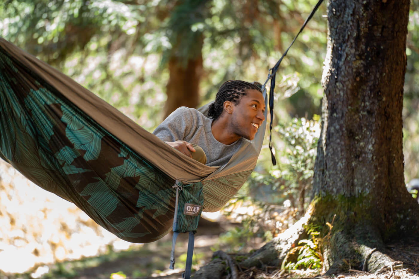 A man lays in a Mountains to Sea DoubleNest Hammock Print while in the woods.