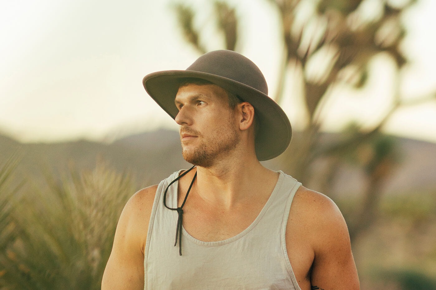 A man wearing a hat, standing in a desert, looks out of frame.