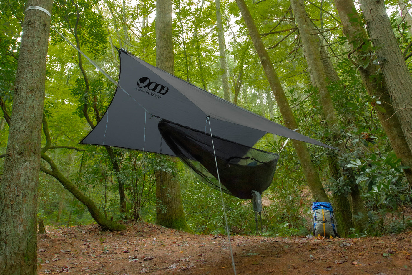 An ENO SubLink Hammock System is hung up in a lush green forest.