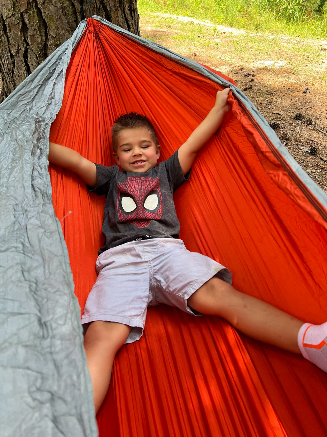 A boy lays in his hammock with his arms and legs spread out. 