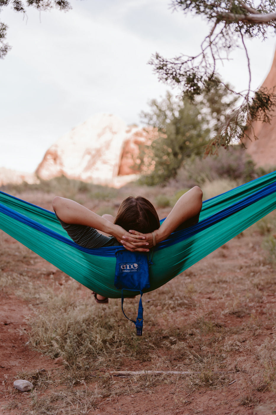 A person sits in an ENO hammock with their arms behind their head relaxing. 