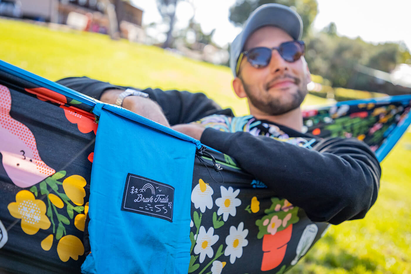 A man sits in a Brave Trails x ENO DoubleNest Print hammock. The focus of the image is on the Brave Trails logo on the hammock. 